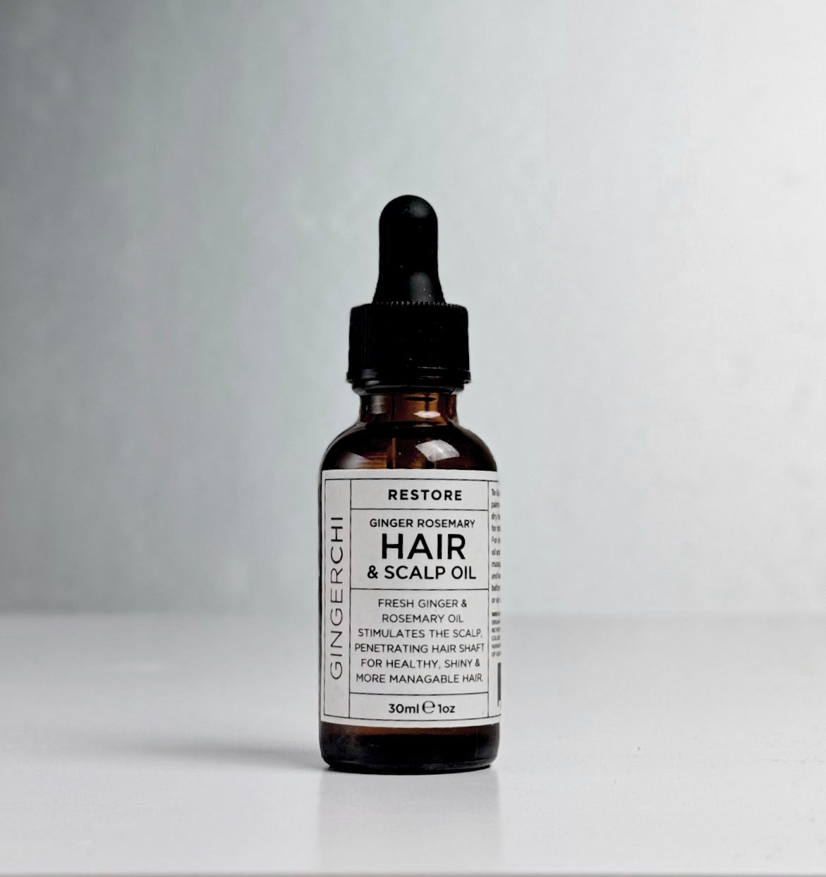 A dropper bottle of Ginger Rosemary Hair & Scalp Oil with a white label on a light background.