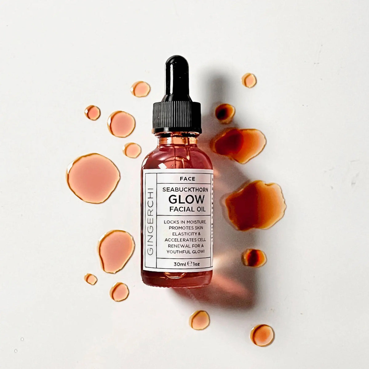 Seabuckthorn Glow Facial Oil bottle with scattered oil spots on white background