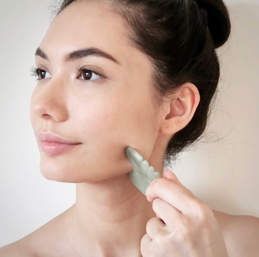 Woman using jade gua sha tool on jawline for skin firming