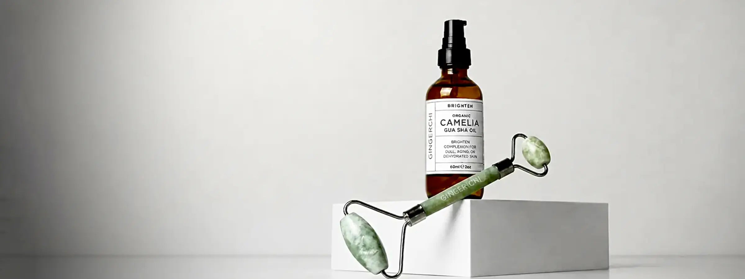 A bottle of Rosemary Hair Growth Treatment with a black spray top and white label, displayed next to a green jade roller on a white block against a light gray background.