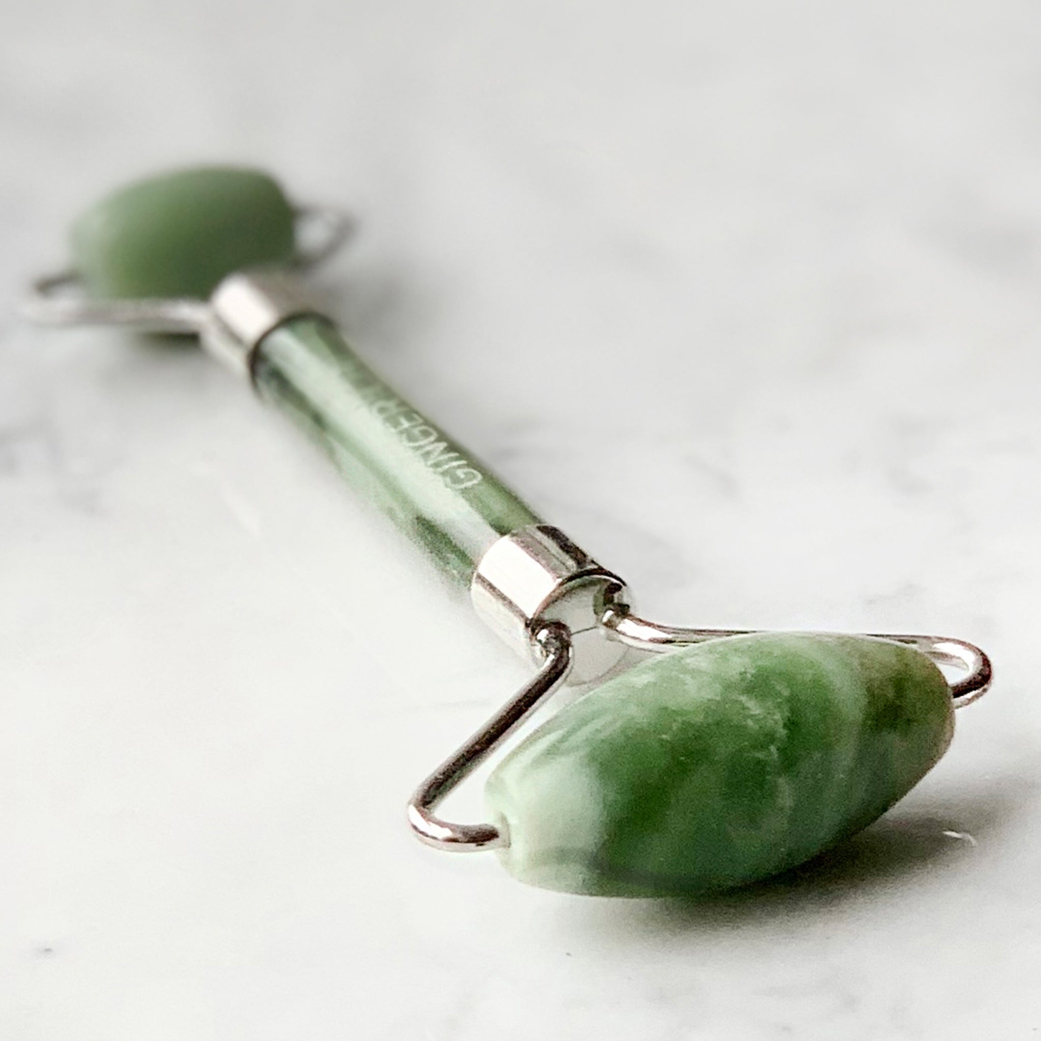 Green jade Gua Sha tool with silver handle on white background
